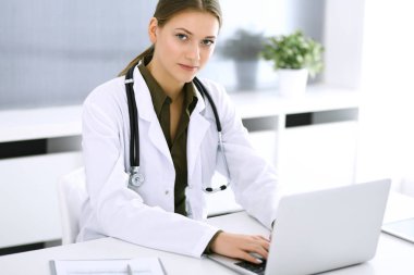 Hastane ofisindeki masada otururken dizüstü bilgisayarda yazan bir doktor. Hekim kadın iş başında. Tıp ve sağlık alanlarındaki veriler