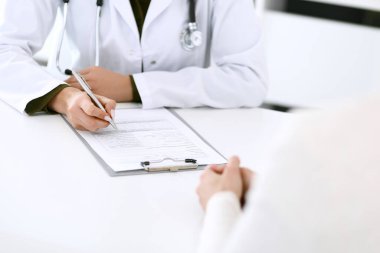 Kadın doktor ve hasta hastane muayenehanesinde oturuyor ve konuşuyor, yakın plan. İlaç kayıtlarını dolduran bir terapist. Tıp ve sağlık hizmetleri kavramı