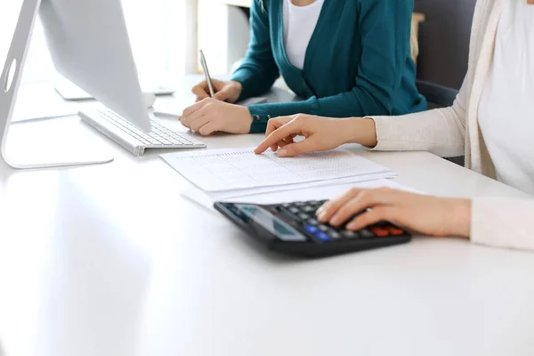 Accountant checking financial statement or counting by calculator income for tax form, hands close-up. Business woman sitting and working with colleague at the desk in office. Audit concept