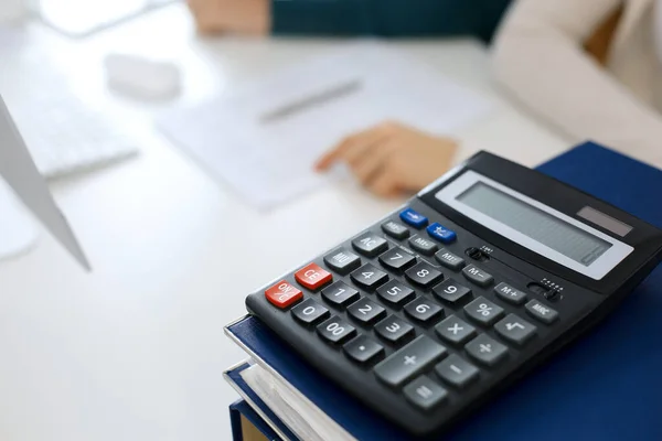 Taschenrechner und Ordner mit Papieren warten darauf, von einer Geschäftsfrau oder Buchhalterin, die am Schreibtisch im Büro arbeitet, verschwommen bearbeitet zu werden. Interne Revision und Steuerkonzept — Stockfoto