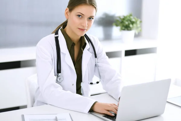 Médico digitando no computador portátil enquanto sentado na mesa no escritório do hospital. Médica no trabalho. Dados em medicina e cuidados de saúde — Fotografia de Stock