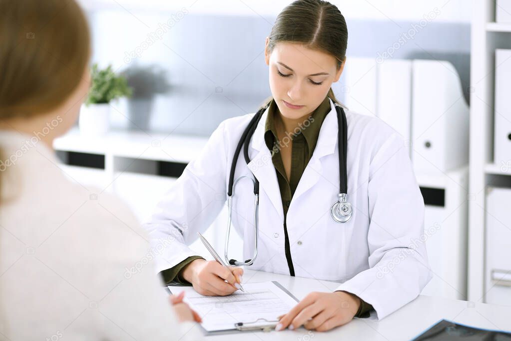 Woman doctor and patient sitting and talking at medical examination at hospital office. Green color blouse suits to therapist. Medicine and healthcare concept