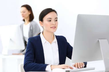 Ofiste bilgisayarla çalışan bir iş kadını, arka planda çalışan bir iş arkadaşı. Masada otururken avukatın ya da muhasebecinin vesikalığı.