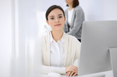 Ofiste bilgisayarla çalışan bir iş kadını, arka planda çalışan bir iş arkadaşı. Masada otururken avukatın ya da muhasebecinin vesikalığı.