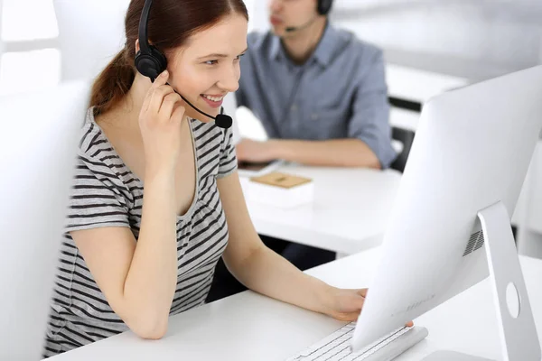 Group of operators at work. Call center. Focus on beautiful woman receptionist in headset at customer service. Business concept and casual striped clothing style — Stock Photo, Image