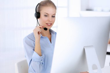 Merkezi ara. İnternette müşterilere danışmak için bilgisayar ve kulaklık kullanan güzel sarışın kadın. Müşteri hizmetleri işgali olarak çalışan bir grup operatör. İş adamları konsepti