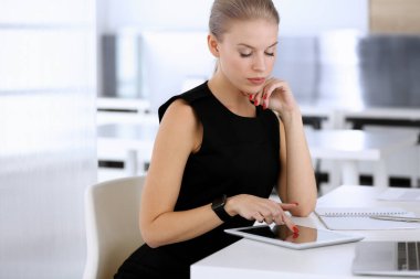 Modern ofisteki masada otururken iş kadını tablet bilgisayarla çalışıyor. Sekreter ya da kadın avukat siyah elbise içinde güzel görünüyor. İş adamları konsepti