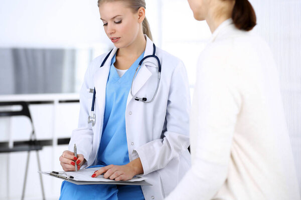 Doctor and patient during consultation. Physician at work filling up medication history record while sitting in emergency hospital, portrait shoot. Medicine and health care concept