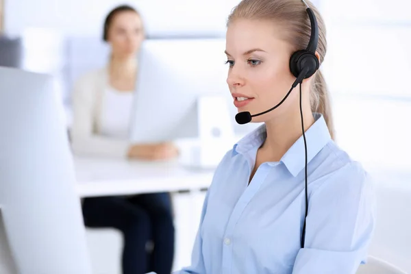 Llama a la oficina central. Hermosa mujer rubia usando computadora y auriculares para consultar a los clientes en línea. Grupo de operadores que trabajan como ocupación de servicio al cliente. Concepto gente de negocios —  Fotos de Stock