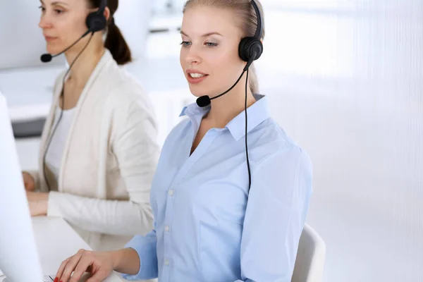 Llama a la oficina central. Hermosa mujer rubia usando computadora y auriculares para consultar a los clientes en línea. Grupo de operadores que trabajan como ocupación de servicio al cliente. Concepto gente de negocios —  Fotos de Stock