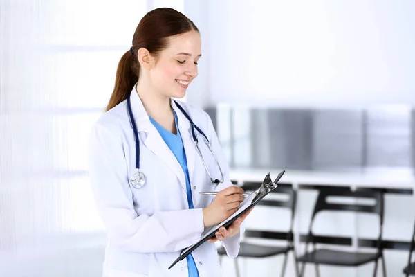 Doctora o estudiante de prácticas en el trabajo. Médico llenando el historial de medicamentos mientras está de pie en la oficina del hospital de emergencia. Concepto de medicina y salud — Foto de Stock