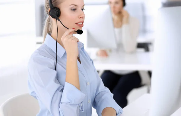 Call center office. Beautiful blonde woman using computer and headset for consulting clients online. Group of operators working as customer service occupation. Business people concept Stock Photo