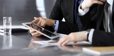 İşadamı tablet bilgisayar kullanıyor ve iş arkadaşı ya da ortağıyla modern ofiste cam masada çalışıyor. Yakın plan. Toplantıda bilinmeyen iş adamları var. Takım çalışması ve ortaklık kavramı