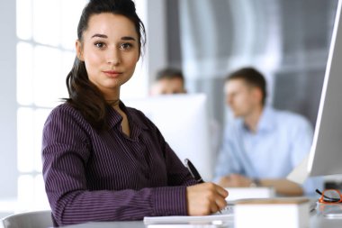 Modern ofisteki işyerinde bilgisayar kullanan bir iş kadını. Esmer sekreter ya da kadın avukat kameraya bakıyor ve mutlu gülümsüyor. Zevk ve başarı için çalışmak