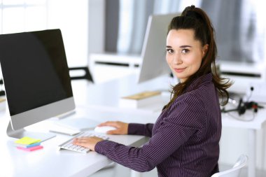 Modern ofisteki işyerinde bilgisayar kullanan bir iş kadını. Esmer sekreter ya da kadın avukat gülümsüyor ve mutlu görünüyor. Zevk ve başarı için çalışmak