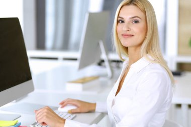 Modern ofisteki işyerinde bilgisayar kullanan bir iş kadını. Sekreter ya da kadın avukat kameraya bakıyor ve mutlu gülümsüyor. Zevk ve başarı için çalışmak