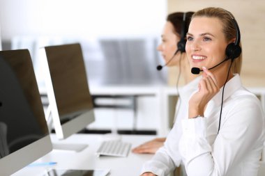 Merkezi ara. İnternette müşterilere danışırken kulaklık kullanan mutlu ve heyecanlı bir iş kadını. Müşteri hizmetleri ofisi ya da tele pazarlama bölümü. İşte gülümseyen operatörler grubu