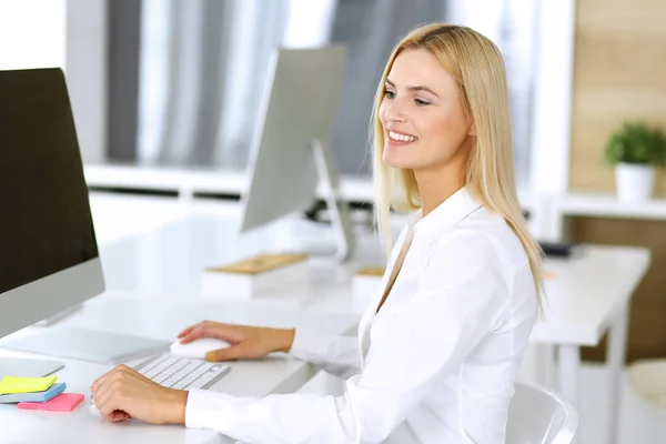 在现代办公室的工作场所使用计算机的女商人。秘书或女律师看着摄像机，开心地微笑着。为快乐和成功而努力 — 图库照片