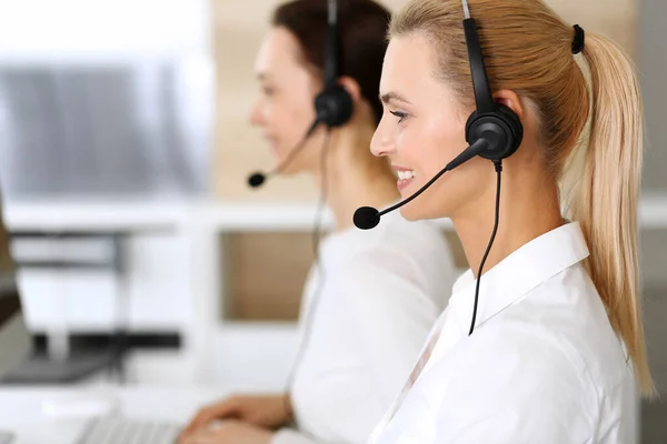 Centro de llamadas. Mujer de negocios feliz y emocionada usando auriculares mientras consulta a clientes en línea. Oficina de servicio al cliente o departamento de telemarketing. Grupo sonriente de operadores en el trabajo — Foto de Stock