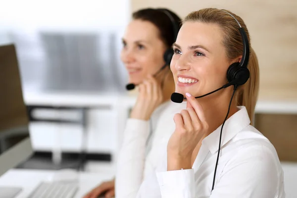 Centro de llamadas. Mujer de negocios feliz y emocionada usando auriculares mientras consulta a clientes en línea. Oficina de servicio al cliente o departamento de telemarketing. Grupo sonriente de operadores en el trabajo — Foto de Stock