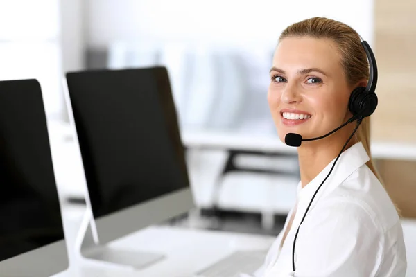 呼叫中心快乐而兴奋的女商人在网上咨询客户时使用耳机。客户服务办公室或电话营销部门.微笑的金发女操作员在工作 — 图库照片