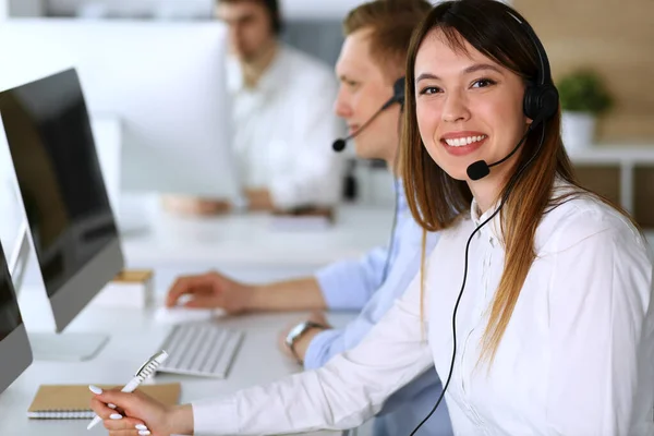 Call center. Group of diverse operators at work. Focus on beautiful asian woman in headset at customer service office. Business concept