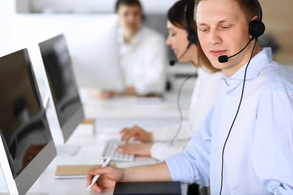 Centro de llamadas. Grupo de operadores diversos en el trabajo. Enfócate en hombre de negocios con auriculares en la oficina de servicio al cliente. Concepto empresarial —  Fotos de Stock