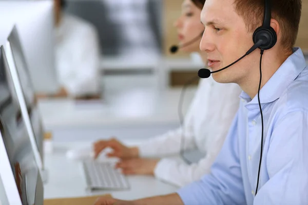 Centro de llamadas. Grupo de operadores diversos en el trabajo. Enfócate en hombre de negocios con auriculares en la oficina de servicio al cliente. Concepto empresarial —  Fotos de Stock