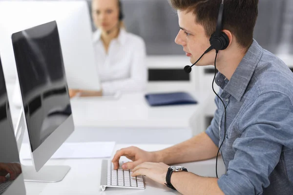 Centro de llamadas. Grupo de operadores vestidos casuales en el trabajo. Enfócate en el joven empresario con auriculares en la oficina de servicio al cliente. Telesales en el negocio —  Fotos de Stock