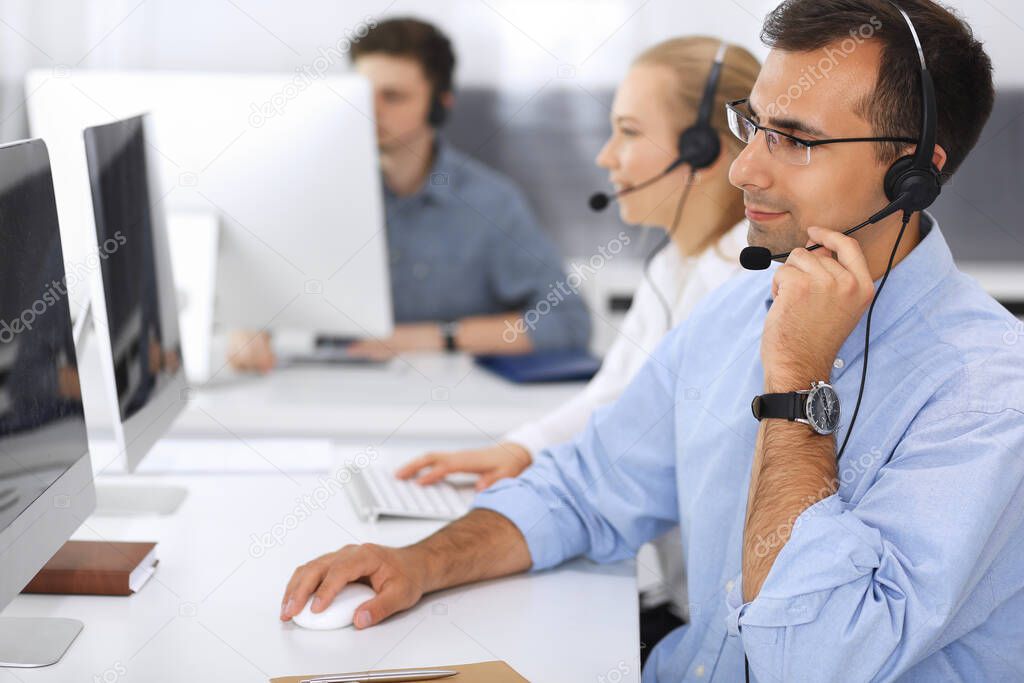 Call center. Group of casual dressed operators at work. Focus on adult businessman in headset at customer service office. Telesales in business