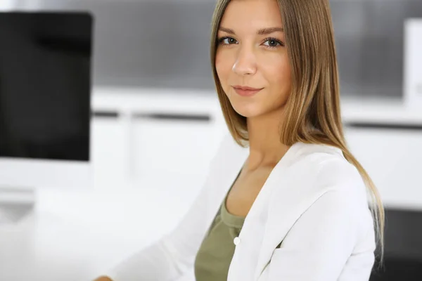 Glada leende affärskvinna sitter vid skrivbordet i moderna kontor. Ung kvinnlig designer eller revisor headshot. Affärsidé — Stockfoto