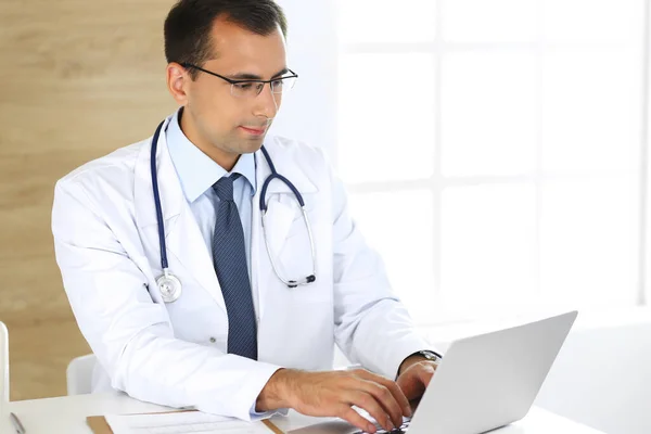 Orvos gépel a laptopján, miközben az asztalánál ül a munkahelyén. Tökéletes orvosi ellátás a klinikán. Orvosi és egészségügyi adatok — Stock Fotó