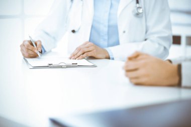 Bilinmeyen kadın-doktor ve kadın hasta klinikteki tıbbi muayenede oturuyor ve konuşuyor, yakın plan. Mavi bluz giyen terapist ilaç geçmişini dolduruyor. Tıp konsepti