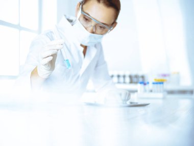 Kadın laboratuvar asistanı mavi sıvıyla test tüpünü analiz ediyor. Tıp, sağlık ve araştırma konsepti