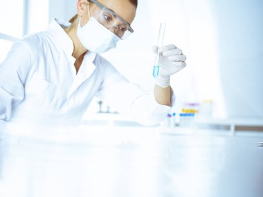 Kadın laboratuvar asistanı mavi sıvıyla test tüpünü analiz ediyor. Tıp, sağlık ve araştırma konsepti