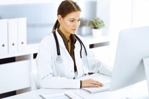 여자 의사가 사무실 책상에 앉아 있는 동안 pc 컴퓨터로 타이핑을 하고 있었어요. 의사가 일하고 있다 — 스톡 사진