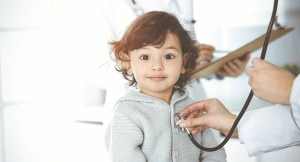 Ženský lékař vyšetřuje dětského pacienta stetoskopem na slunné klinice. Roztomilé arabské batole na návštěvě lékaře — Stock fotografie