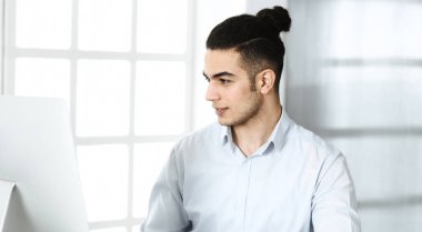 İşadamı modern ofiste bilgisayarla çalışıyor. Arap erkek girişimcinin iş yerindeki portresi. İş konsepti