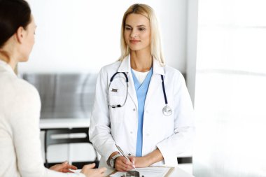 Hastanedeki doktor kadın hastaya danışmaktan mutlu ve heyecanlı. Sarışın doktor ilaç kayıtlarını ve sınav sonuçlarını pano kullanarak kontrol ediyor. İlaç ve sağlık hizmetleri