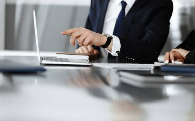 Bilinmeyen iş adamları ve kadınlar oturmuş, dizüstü bilgisayarlarını kullanıyorlar ve modern ofiste buluşmada soruları tartışıyorlar, yakın plan.