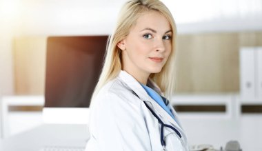 Güneşli klinikte masa başında oturan kadın doktor. Sarışın, neşeli doktor yardıma hazır.