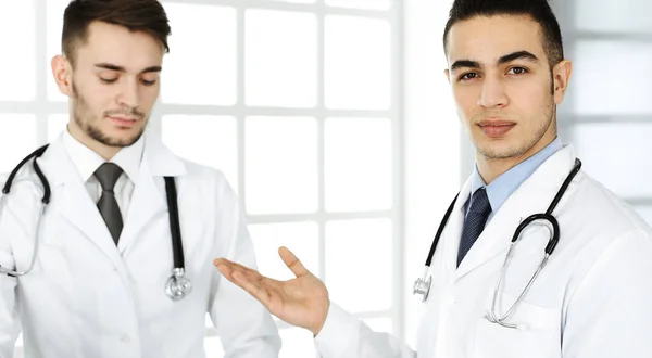 Arabische arts die aan het glazen bureau zit met een blanke collega in een medisch kantoor of kliniek. Verscheidene artsen team, geneeskunde en gezondheidszorg concept — Stockfoto