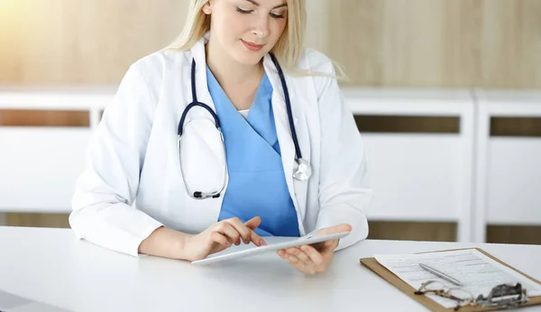 Kvinna-läkare på jobbet medan du sitter vid skrivbordet i solig klinik. Blond glad läkare fylla upp medicinhistoria rekord form — Stockfoto