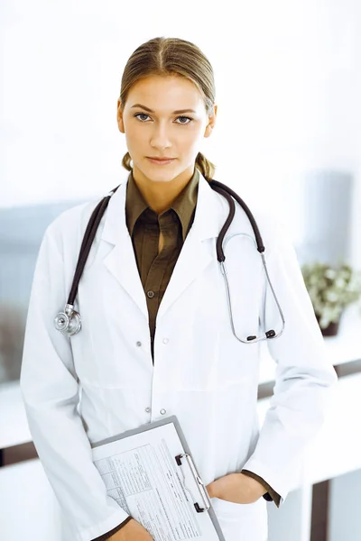 Žena-doktorka stojí a dívá se do kamery. Perfektní lékařská služba na klinice — Stock fotografie