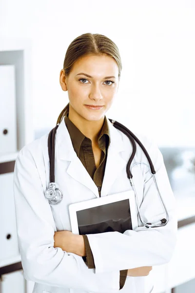 Женщина-врач стоит и смотрит в камеру. Идеальное медицинское обслуживание в клинике — стоковое фото