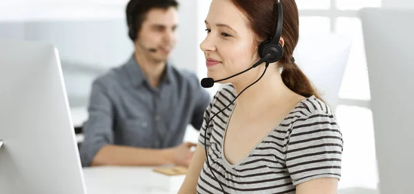 Mujer joven vestida casual usando auriculares y computadora mientras habla con los clientes en línea. Grupo de operadores en el trabajo. Call center, concepto de negocio —  Fotos de Stock