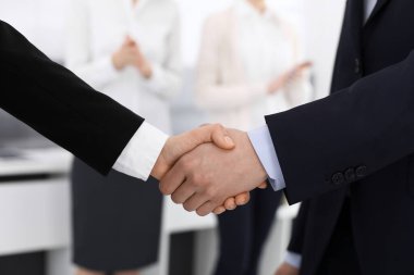 İş adamı ve kadın arka planda iş arkadaşlarıyla tokalaşıyor. Ofiste tokalaşırken. İş hayatında başarı kavramı