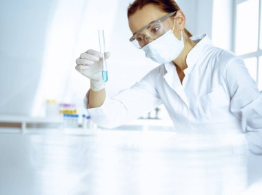 Kadın laboratuvar asistanı mavi sıvıyla test tüpünü analiz ediyor. Tıp, sağlık ve araştırma konsepti