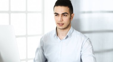 İşadamı modern ofiste bilgisayarla çalışıyor. Arap erkek girişimcinin iş yerindeki portresi. İş konsepti