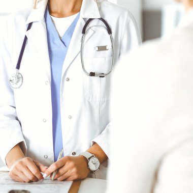 Bilinmeyen kadın doktor oturuyor ve kadın hastayla iletişim kuruyor. Doktor tıbbi geçmişi ve muayene sonuçlarını yakından kontrol ediyor. Sağlık hizmetleri kavramı